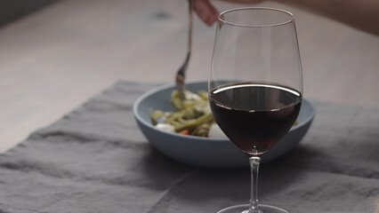 man eatings fettuccine with pesto, tomatoes and mozzarella with glass of red wine