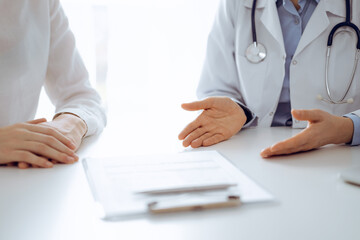Doctor and patient discussing current health questions while sitting near of each other and using clipboard at the table in clinic, just hands closeup. Medicine concept