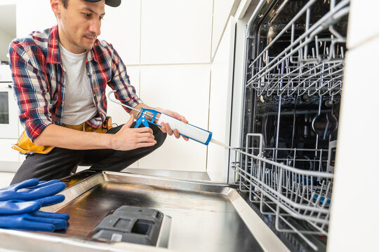 Process of dishwashing machine installation. Young African service man setting up dishwasher in new stylish kitchen. Diverce handyman in workwear, close portrait.