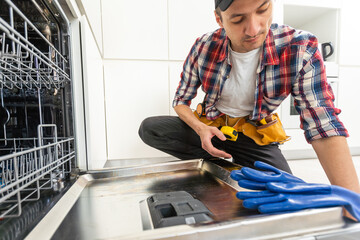 Repairman examining dishwasher with toolbox in kitchen