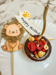 A small brownie chocolate cake on a plate with a golden candle and an axe with the inscription happy birthday, a cardboard lion