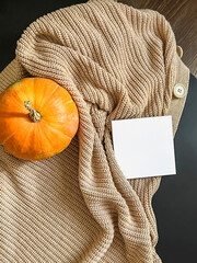 A cozy composition with an orange pumpkin, a beige sweater on a black table, and a place for text. Top view. copy space