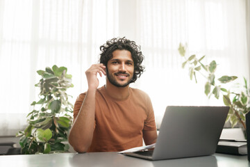 Cheerful student diligently working on his laptop, seated at a table in a cozy room
