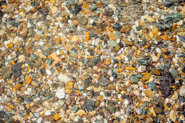 Pebbles at the bottom of a clear river. Colorful stone underwater pattern. Abstract natural background, mock up for design, copy space.