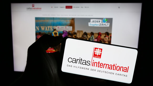 Stuttgart, Germany - 10-08-2023: Person holding cellphone with logo of aid agency Caritas International in front of webpage. Focus on phone display.