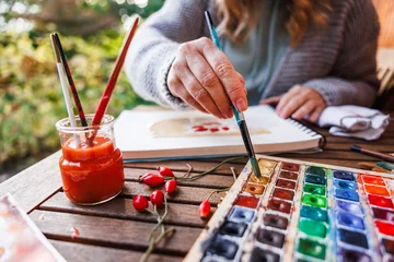 Muurstickers Woman artist dips paintbrush into color palette and painting a watercolor illustration © encierro