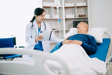 Obraz premium Asian doctor in white suit take notes while discussing and Asian elderly, man patient who lying on bed with receiving saline solution in hospital .