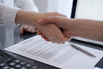 Business people shaking hands above contract papers just signed on the grey table, close up. Lawyers or entrepreneurs at meeting. Teamwork, partnership, success concept