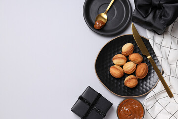 Cookie nuts on plate, condensed milk in glass, gift boxes and hand on light background