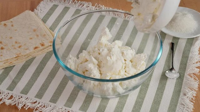 The girl's hands pour cottage cheese, sugar, vanillin into a glass plate and mix to prepare the curd filling