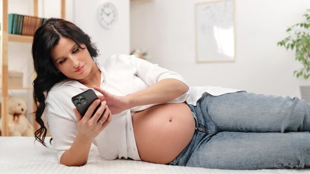 Relaxed pregnant woman future mother use smartphone searching information lying white carpet floor
