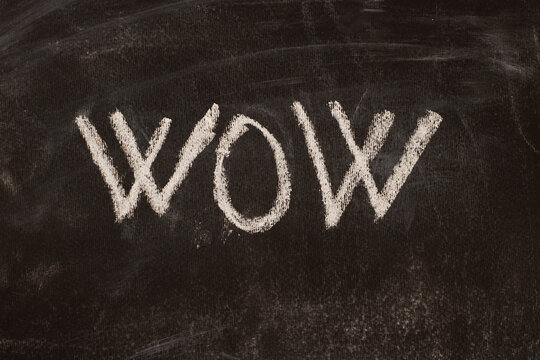 The word wow written in white chalk on a black chalkboard, message.