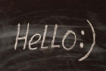 The word hello with an emoticon written on a black chalkboard in chalk.