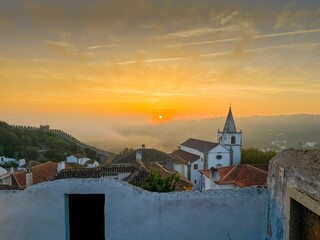 the sun is rising over the rooftops of small buildings
