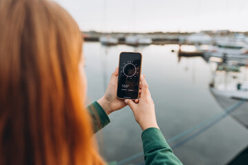 Concept a Hand Holding a Compass on smart phone. Young Woman Searching locations, walking along the waterfront, seaside.