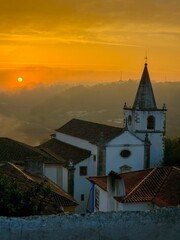 Fototapeta premium a sunset over a large white church surrounded by mountains and trees