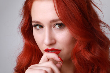 Close-up of stunning young woman with long red hair posing on white background.