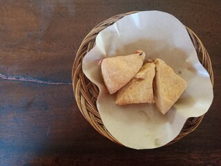 Fried tofu served on a rattan plate with waxed paper on a wooden table.