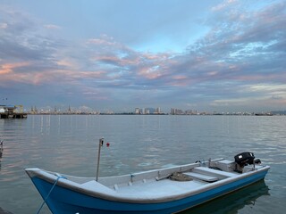 A small boat is moored on the riverbank. With tall buildings in the background reflecting the water surface.