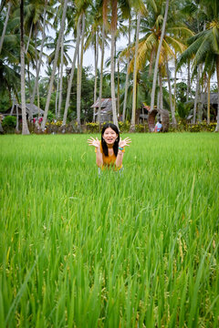 A girl pretends to be cute, and half squats in a green paddy field.