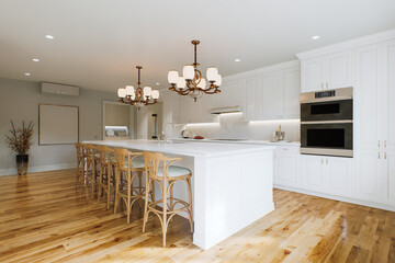 Traditional white kitchen with long island and wooden chairs with varnished wood flooring. 
