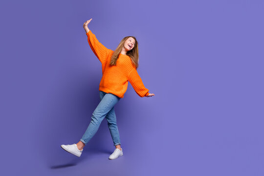 Full length photo of dreamy excited teenager girl orange sweater with jeans flying arms look novelty isolated on violet color background