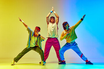 Stylish three men in colorful sportswear posing against gradient yellow blue background in neon...