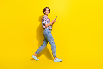 Fototapeta na wymiar Full size profile photo of nice positive girl use smart phone walking empty space isolated on yellow color background