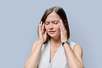 Young woman experiencing stress headache, on gray background