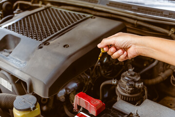 Hand of woman check the oil level in car engine. Self service woman's hand use dipstick checking...