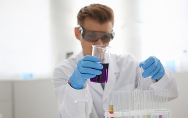 A male chemist holds test tube of glass in his hand overflows a liquid solution of potassium...