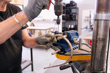 repairer of brass musical instruments using a vertical drill to restore the tubing of a French horn in a luthier shop