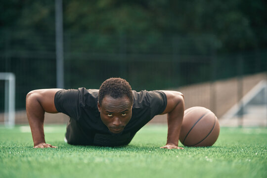Doing push ups. Young black man is with basketball ball outdoors