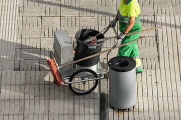 Sweeper worker pushing a cart on a city sidewalk