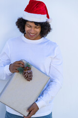 young latino man in a Santa hat and white t-shirt looking at a simple silver gift with a pineapple as decoration.