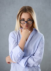 Portrait of a sexy woman in a man's shirt wearing glasses on a gray background looks at the camera....