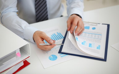 Male hands hold documents with financial statistics at office workspace closeup. White collar check...