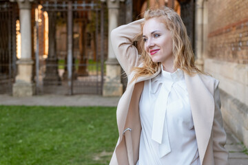 Fototapeta premium Portrait of attractive red-haired girl in spring outdoors. Cute blonde girl in white blouse and coat outside smiling and looking at the camera