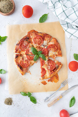Pizza margherita with basil on a white background. Pizza with cheese and tomatoes cut into pieces. Homemade baking.
