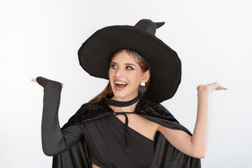 Fototapeta premium Happy surprised young woman in black clothes and black hat raised her palms up. Joyful smiling girl. White background. Halloween party.
