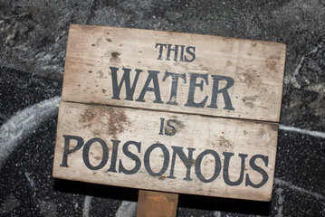 Wooden sign with writing stating this water is poisonous.