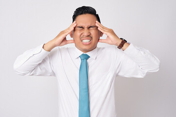 Unhealthy young Asian businessman wearing formal shirt and tie suffering from headache or migraine, massaging his temples with closed eyes isolated on white background