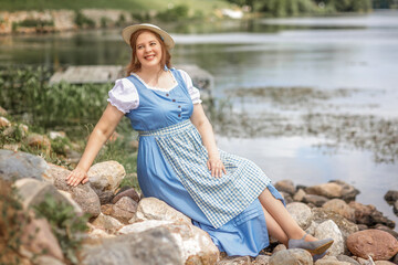 A beautiful retro woman in a blue dress and hat outdoors on the riverbank.