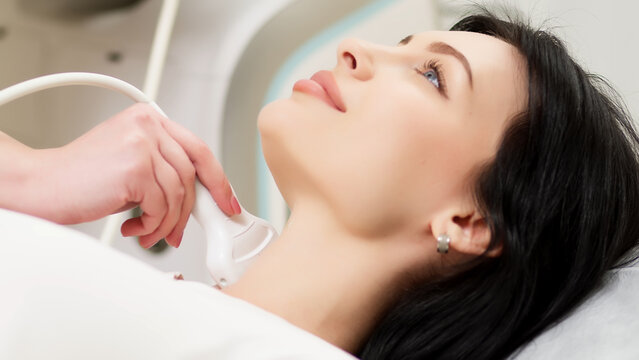 A doctor diagnoses a patient's thyroid gland using an ultrasound scanner. A woman holds an ultrasound probe along a patient's neck in a clinic.