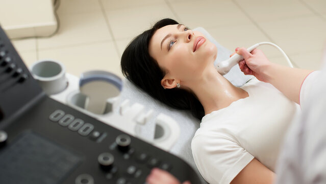 A doctor performs an ultrasound of the thyroid gland and cervical lymph nodes on a patient in a modern clinic against a light background. Advertising of modern medicine and technology
