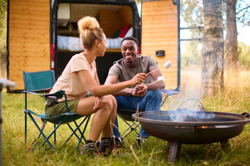 Couple Camping In Countryside With RV Toasting Marshmallows Outdoors On Fire