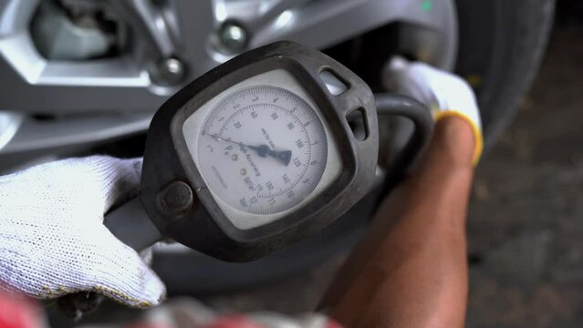Mechanic wearing gloves checking tire pressure with the compressor at the service station, car repair. Professional tire fitting at car service