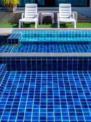 Couple white sunbeds on the green glass at swimming pool with clean clear water, nobody, vertical...