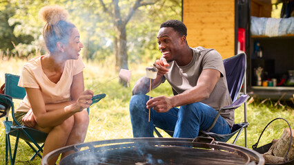 Man Burning Marshmallows On Outdoor Fire As Couple Camp In Countryside With RV