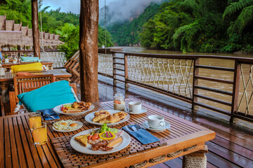breakfast table at a tropical beach house on the River Kwai in Thailand.Wooden floating raft house in river Kwai Kanchanaburi, Thailand, breakfast with eggs bread and coffee - obrazy, fototapety, plakaty